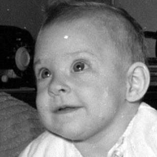 Baby in white clothing lying on a blanket.