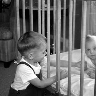Young child looking at an infant in a crib.