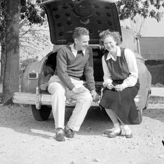 Man and woman sitting on a vintage car bumper.