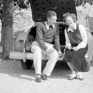 Man and woman sitting on a vintage car bumper.