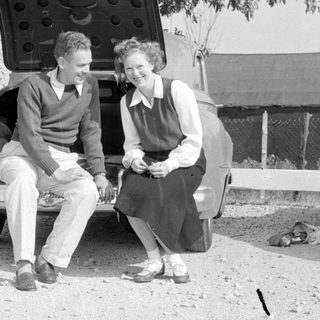 Man and woman sitting on a vintage car bumper.