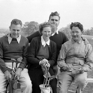 Four people posing with golf equipment outdoors.