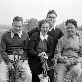 Four people posing with golf equipment outdoors.