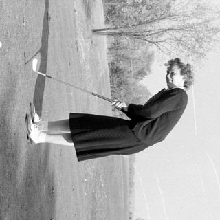 Woman in vintage attire playing golf on a course.