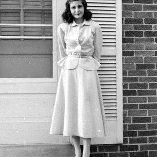 Woman in a peplum dress standing by a door.