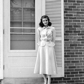 Woman in a peplum dress standing by a door.