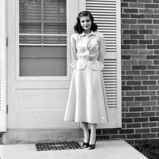 Woman in a peplum dress standing by a door.