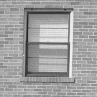 Man in dress shirt squatting in front of brick building.