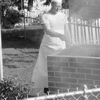 Person in chef attire at a brick grill.