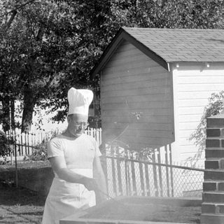 Person in chef attire at a brick grill.