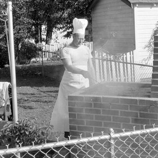 Person in chef attire at a brick grill.