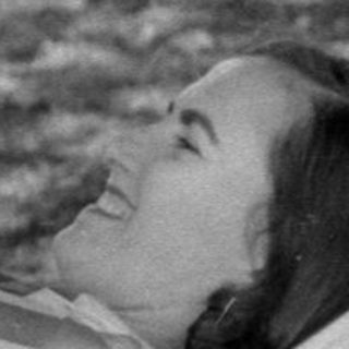 Man standing beside a woman lying on a cot.