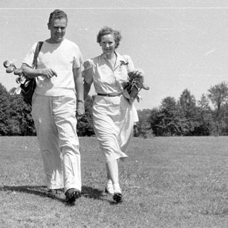 Man and woman walking in a grassy field.