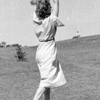 Woman in a dress swinging a golf club.
