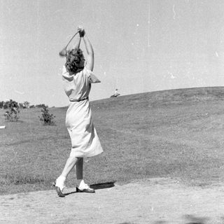 Woman in a dress swinging a golf club.