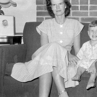 Three people sitting on a sofa before a fireplace.