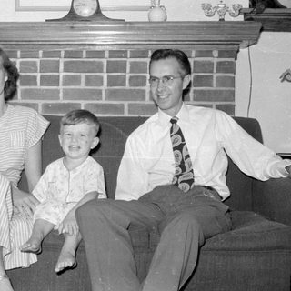 Three people sitting on a sofa before a fireplace.
