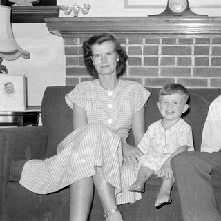 Three people sitting on a sofa before a fireplace.