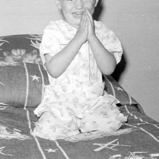 Child in pajamas sitting on a ship-print bedspread.