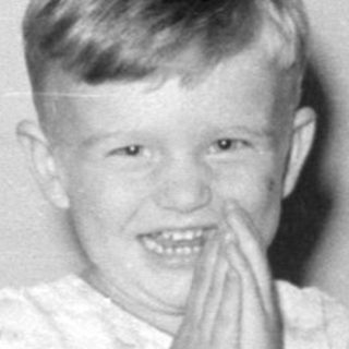 Child in pajamas sitting on a ship-print bedspread.