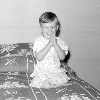 Child in pajamas sitting on a ship-print bedspread.