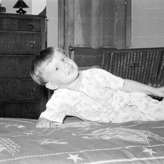 Child in light pajamas lying on a patterned bed.