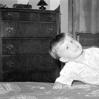 Child in light pajamas lying on a patterned bed.