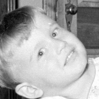 Child in light pajamas lying on a patterned bed.
