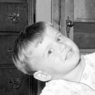 Child in light pajamas lying on a patterned bed.