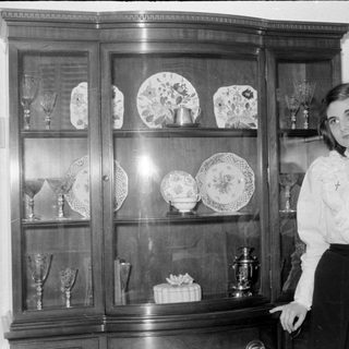 Woman standing beside a china cabinet with decorative plates.