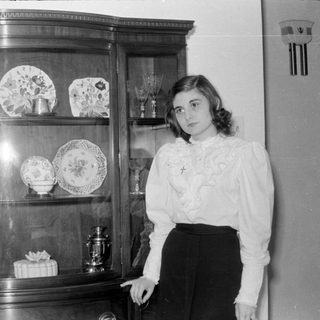 Woman standing beside a china cabinet with decorative plates.