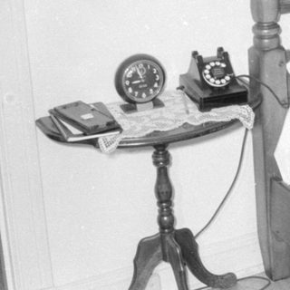 Woman on rotary phone sitting on a bed.