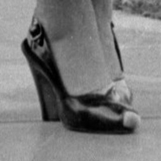 Woman in a ruffled dress standing by a house.