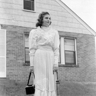 Woman in a ruffled dress standing by a house.