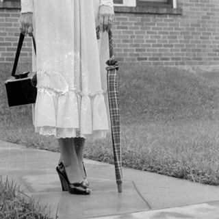 Woman in a ruffled dress standing by a house.