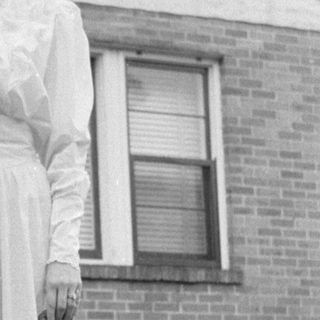 Woman in a ruffled dress standing by a house.