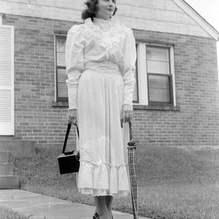Woman in a ruffled dress standing by a house.