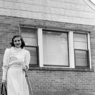 Woman in ruffled dress standing before a brick house.