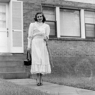 Woman in ruffled dress standing before a brick house.