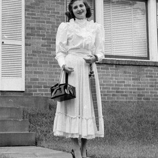Woman in a dress standing before a brick house.