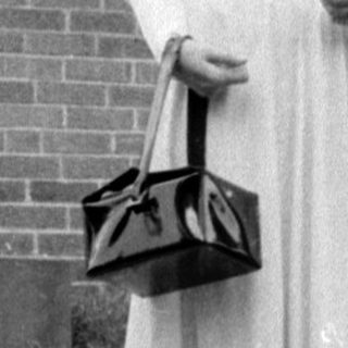 Woman in a dress standing before a brick house.