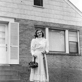 Woman in a dress standing before a brick house.