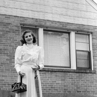 Woman in a dress standing before a brick house.