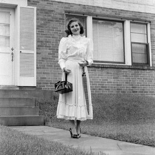 Woman in a dress standing before a brick house.