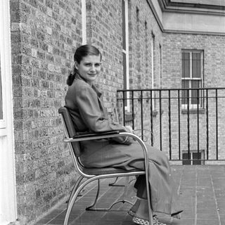 Woman in a suit sitting on a tiled terrace.
