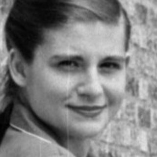 Woman in a suit sitting on a tiled terrace.