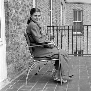 Woman in a suit sitting on a tiled terrace.