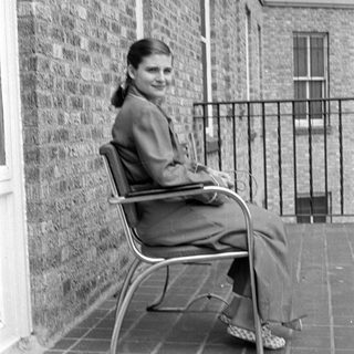 Woman in a suit sitting on a tiled balcony.