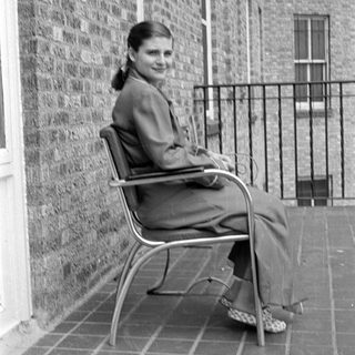 Woman in a suit sitting on a tiled balcony.
