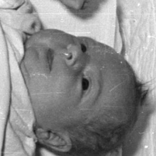 Infant lying in a quilted white bassinet.